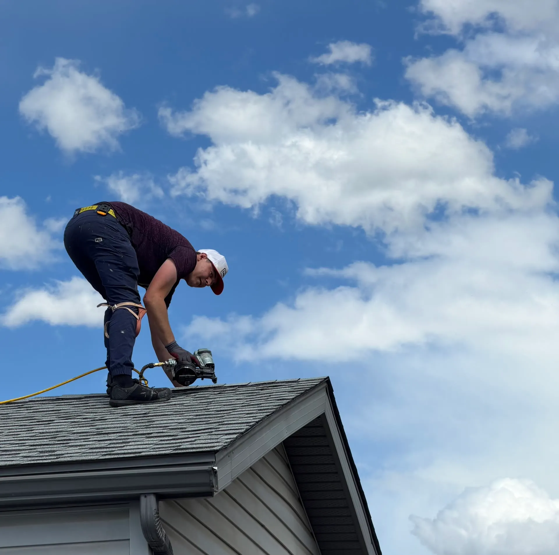 Roofer fastening asphalt shingles on a roof ridge against a blue Calgary sky